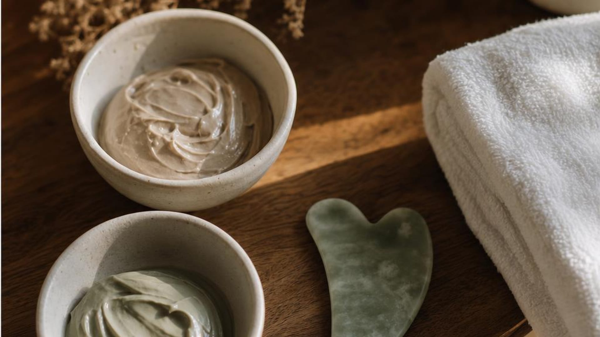Clay mask bowls beside a jade gua sha stone and white towel