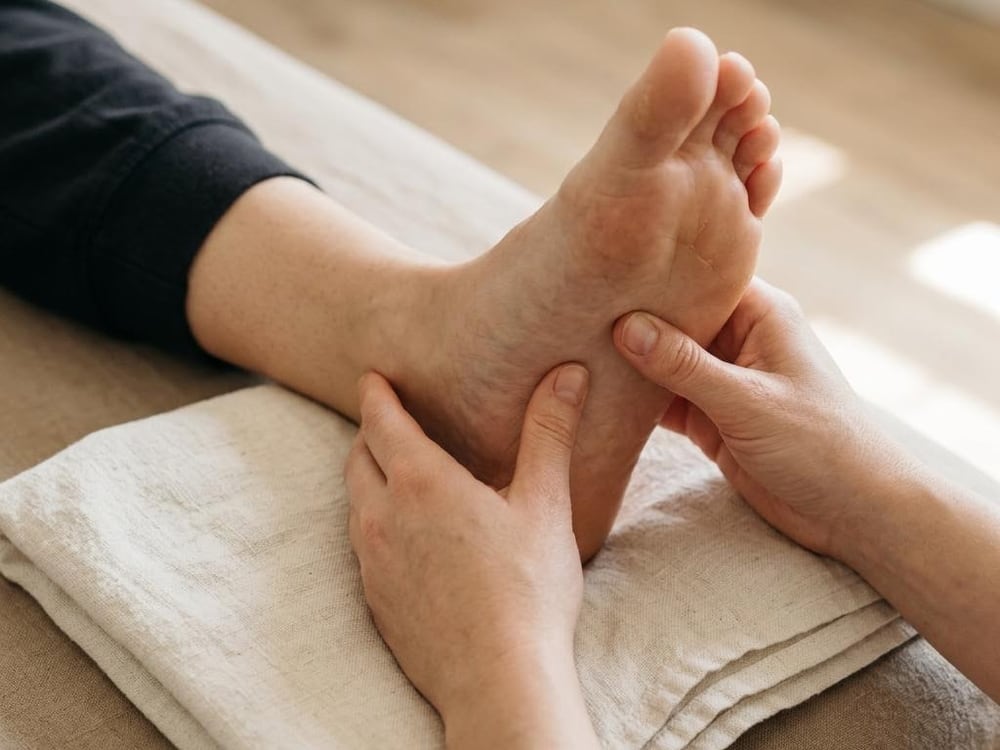 Hands massaging the sole of a foot over a folded ivory towel