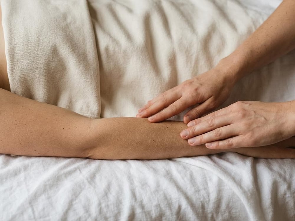 Hands resting lightly along a forearm on white linen