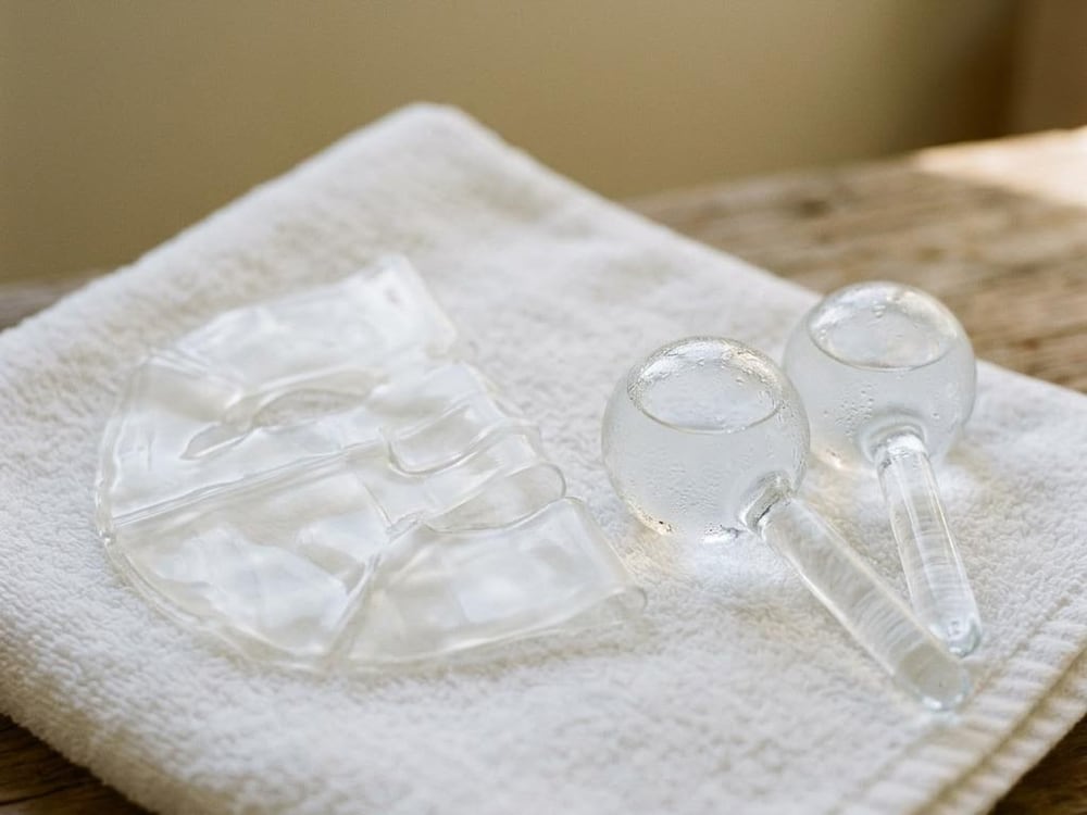 A translucent hydrogel mask beside two glass facial globes on a white towel