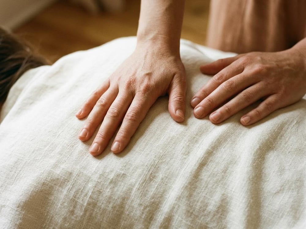 Hands applying palm pressure to an upper back covered in ivory linen