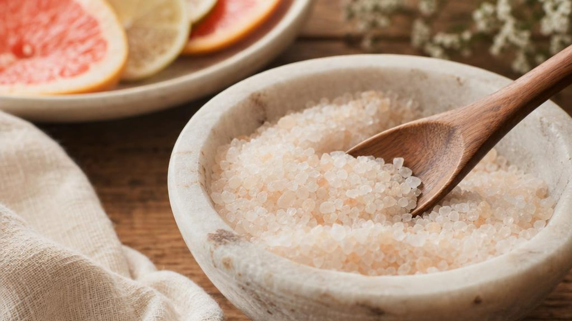 Salt scrub, wooden spoon, citrus slices, and a towel