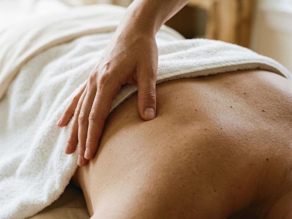 A thumb pressing beside a shoulder blade above a white towel