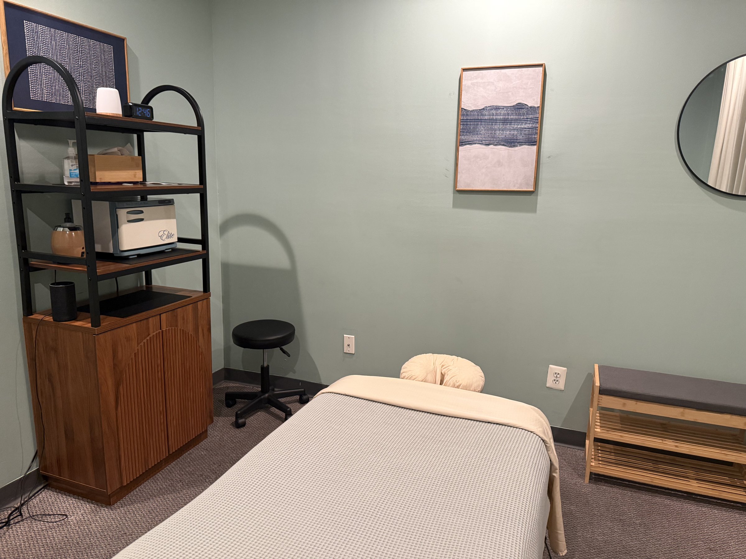 Bright treatment room with a massage table and wood shelving